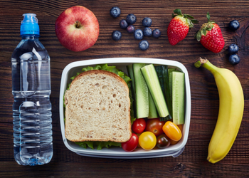 A balanced nutritious packed lunch of a sandwich, fruits, vegetable, and water