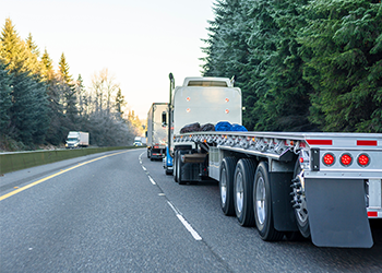 Commercial semi trucks lined up on tree-lined highway