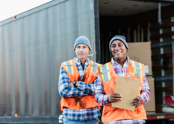Two employees wearing safety vests in front of an open trailer with boxes inside