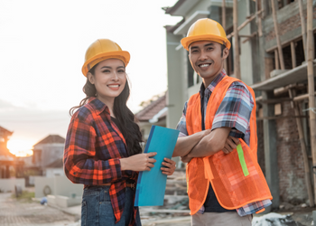 Two workers at a construction site smiling during sunset