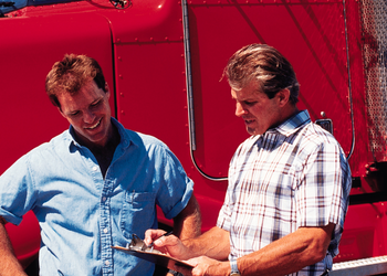 Two men looking at a clipboard in front of a red semi truck