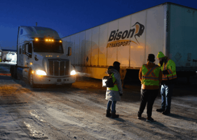 Three workers wearing safety vests with the CTPS Bison Trucks in a snowy lot